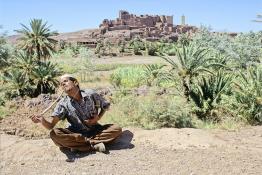 Image du Maroc Professionnelle de  Le paysage, formé par la kasbah Tifoultoute qui se dresse majestueusement sur un éperon rocheux qui domine la vallée de l'oued Ouarzazate, attire les touristes qui prennent le temps de s'arrêter pour prendre une photo. Précisément à cet endroit un charmeur de serpent tenant une vipère avec sa main droite tout en surveillant le mouvement du scorpion noir qu’il avait accroché à son cou avec sa main gauche pose aux touristes contre un billet avec derrière lui comme décor celui qui avait servit pour de grand films comme Lawrence d’Arabie et Jésus de Nazareth à quelque kilomètres de la ville de Ouarzazate au sud du Maroc le Samedi 23 Août 1997. (Photo / Abdeljalil Bounhar)
 